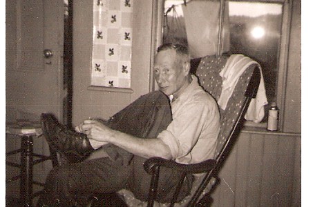 Older man with sunburn face sitting on a rocking chair inform of a window, tying one shoe